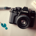 Close-up of Canon AE-1 Program camera with repair tools and lubricant on gray background